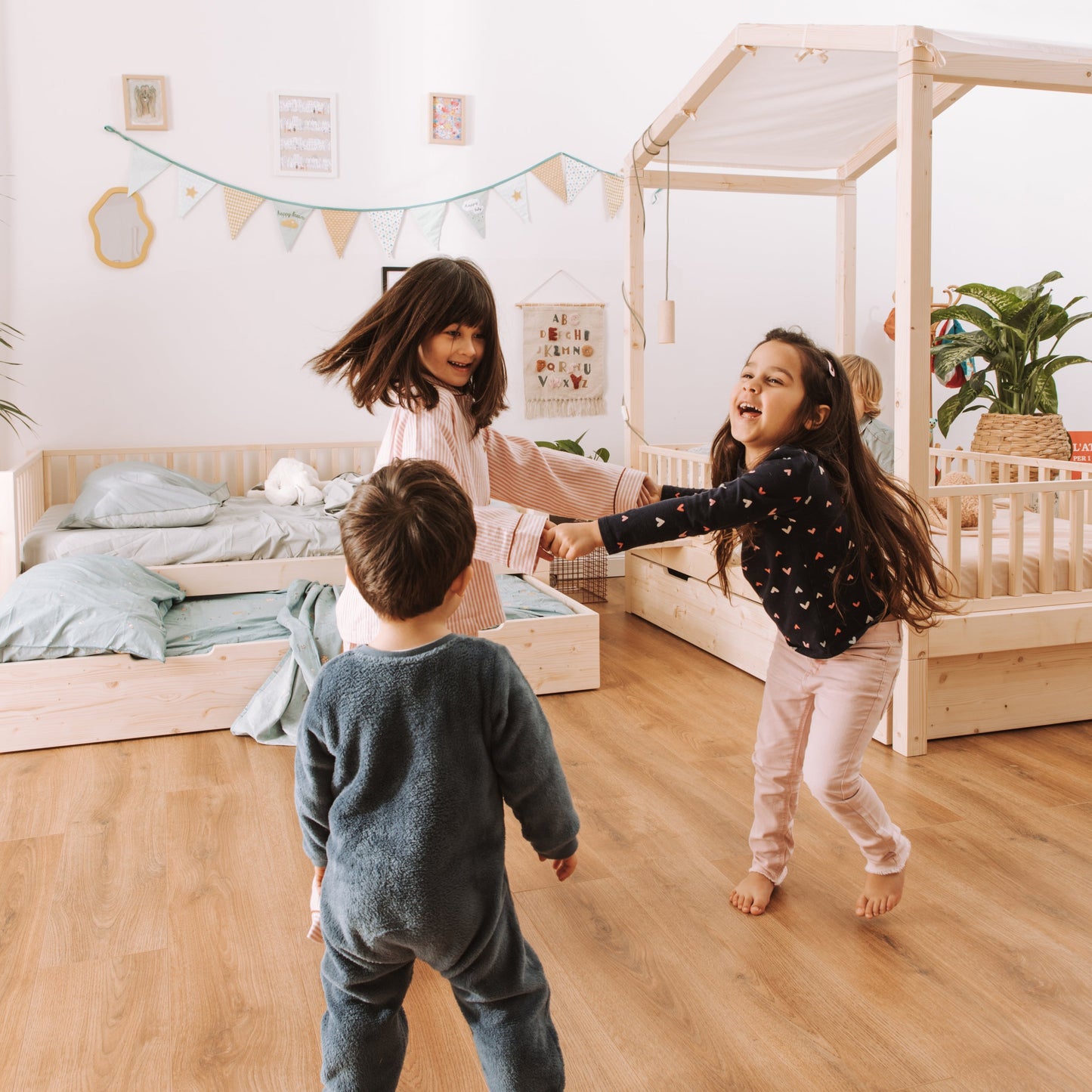 bambini di diverse età giocano in una cameretta con lettini montessoriani con baldacchino, cassettone letto e barriere protettive