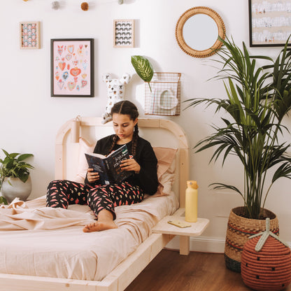 bambina legge sdraiata su letto in legno naturale con comodino gamma zero+ 