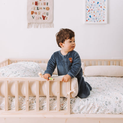 bambino su letto montessoriano con cuscino paracolpi e barriere protettive in legno naturale