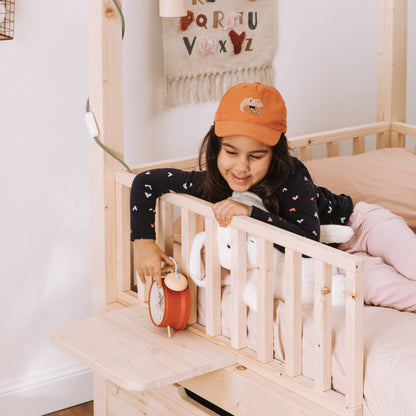 bambina appoggia una sveglia su comodino in legno naturale per letto montessoriano nabè